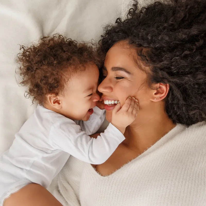 A mother and her toddler laughing together, cheek to cheek