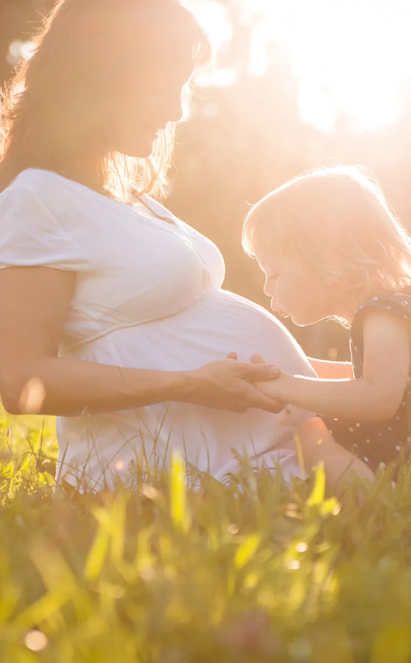 A pregnant mother and her young daughter in a sunlit field